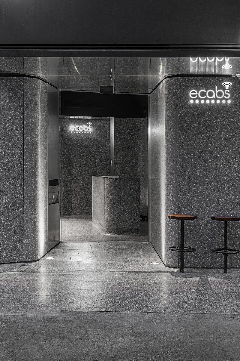 Exterior entrance to the Ecabs office featuring curved terrazzo-clad walls, recessed lighting, and a compact reception area visible through the open doorway.