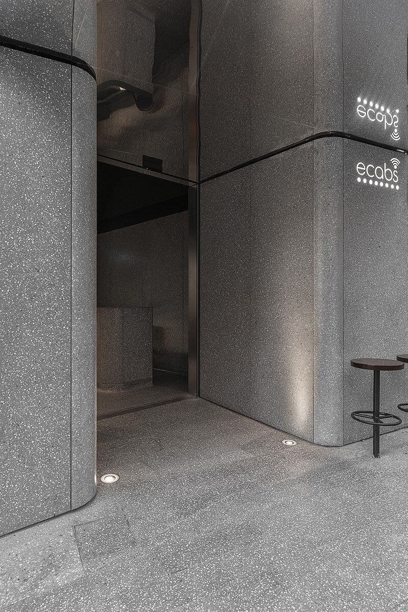 Corner perspective of the Ecabs reception entrance, highlighting the dark grey terrazzo cladding from the Minima Collection and minimal street furniture.