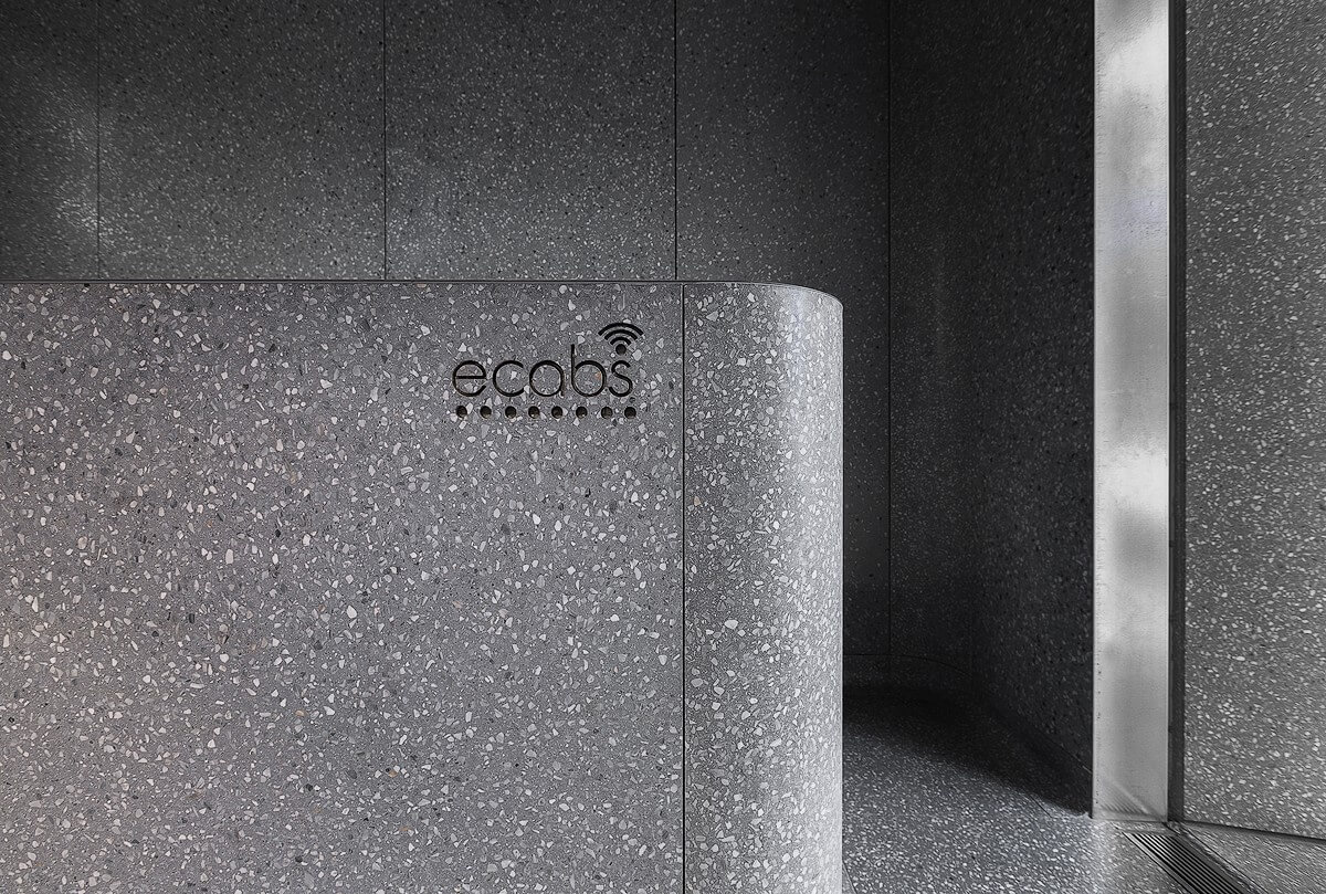 Close-up view of the Ecabs reception desk clad in honed 'Smoke Dark Grey' terrazzo with the Ecabs logo etched into the rounded front panel.