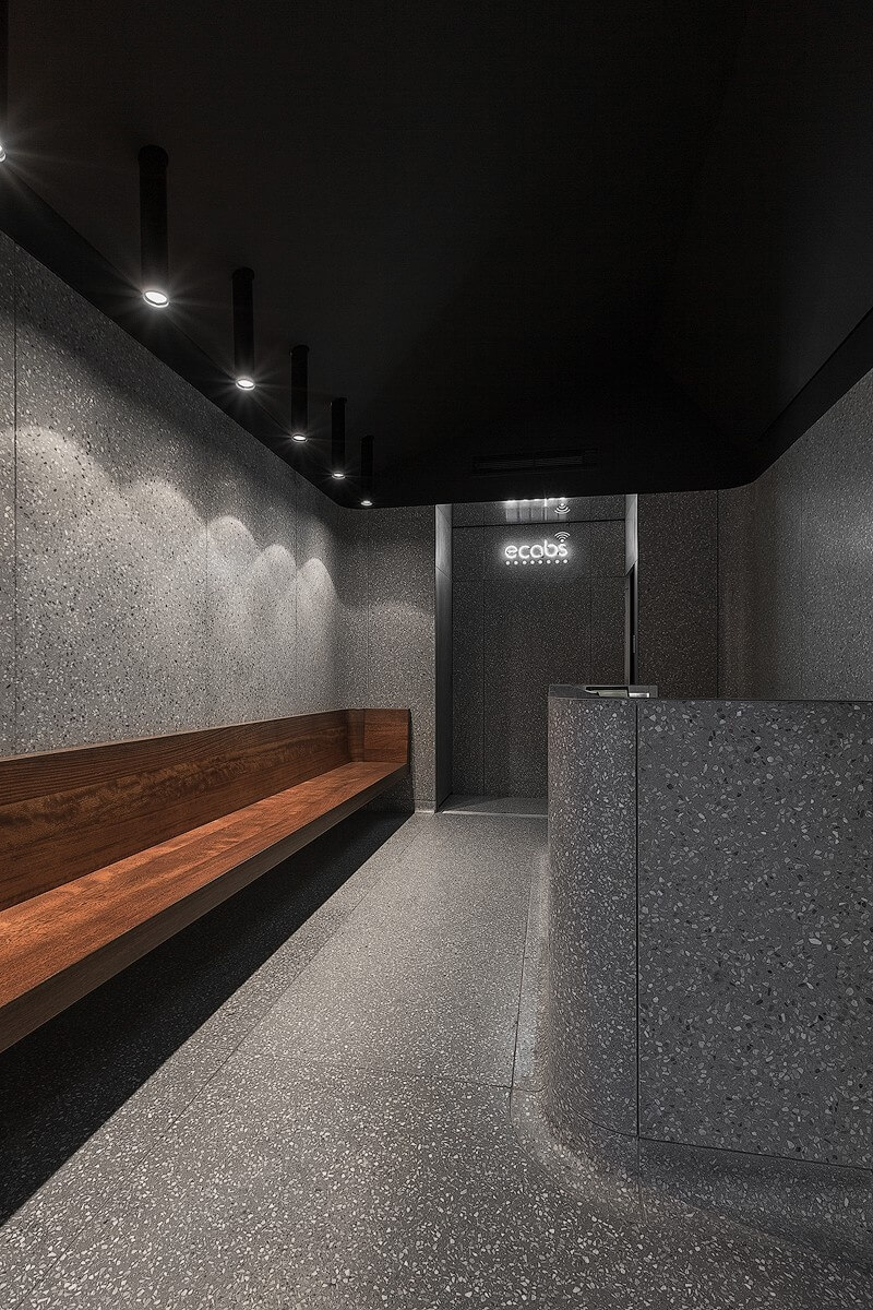 Interior shot of the Ecabs waiting area featuring a long walnut bench, terrazzo flooring and walls, and a reception desk beneath a black ceiling with spotlights.