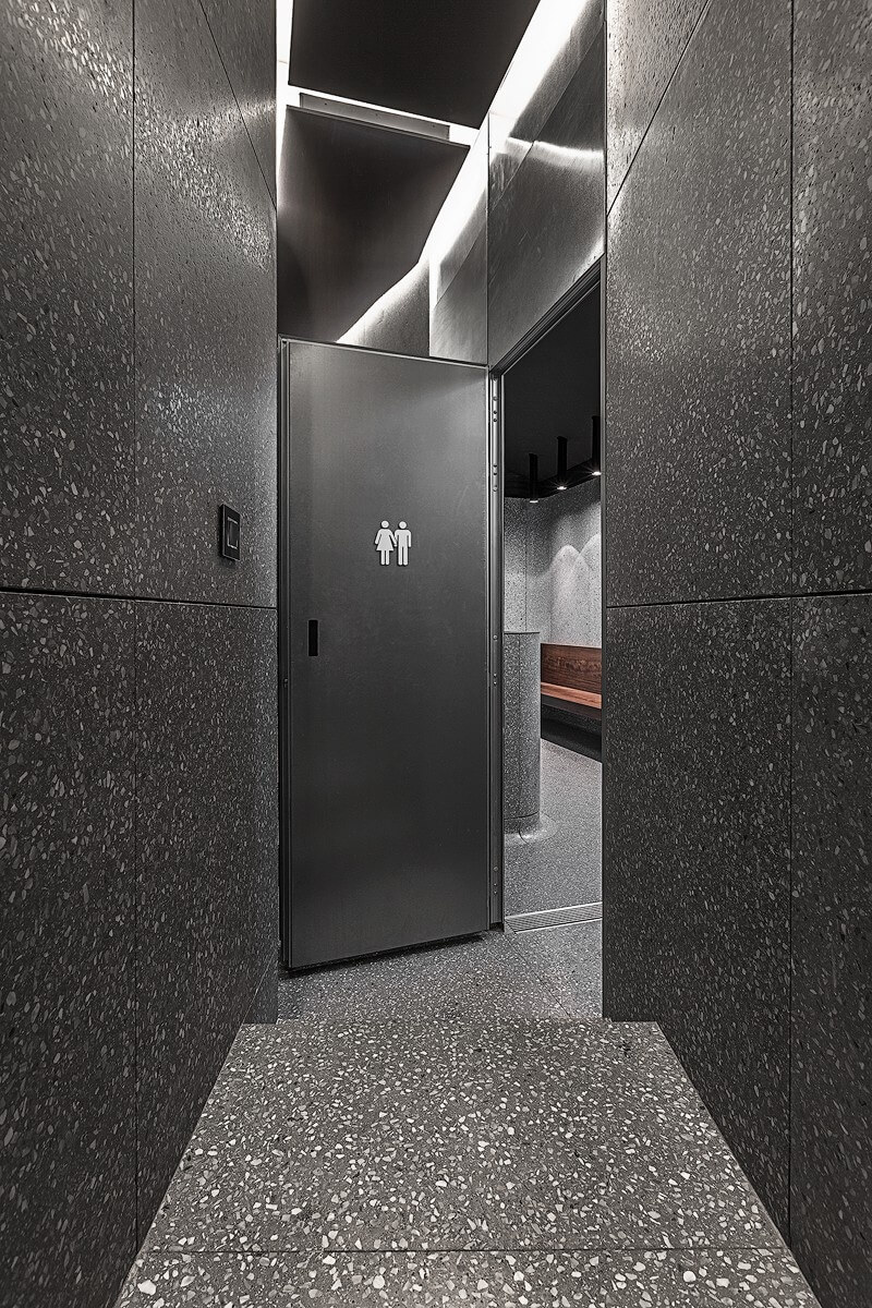 Interior hallway leading to a restroom at Ecabs, featuring dark terrazzo walls, steps, and a partially open door with male and female restroom signage.