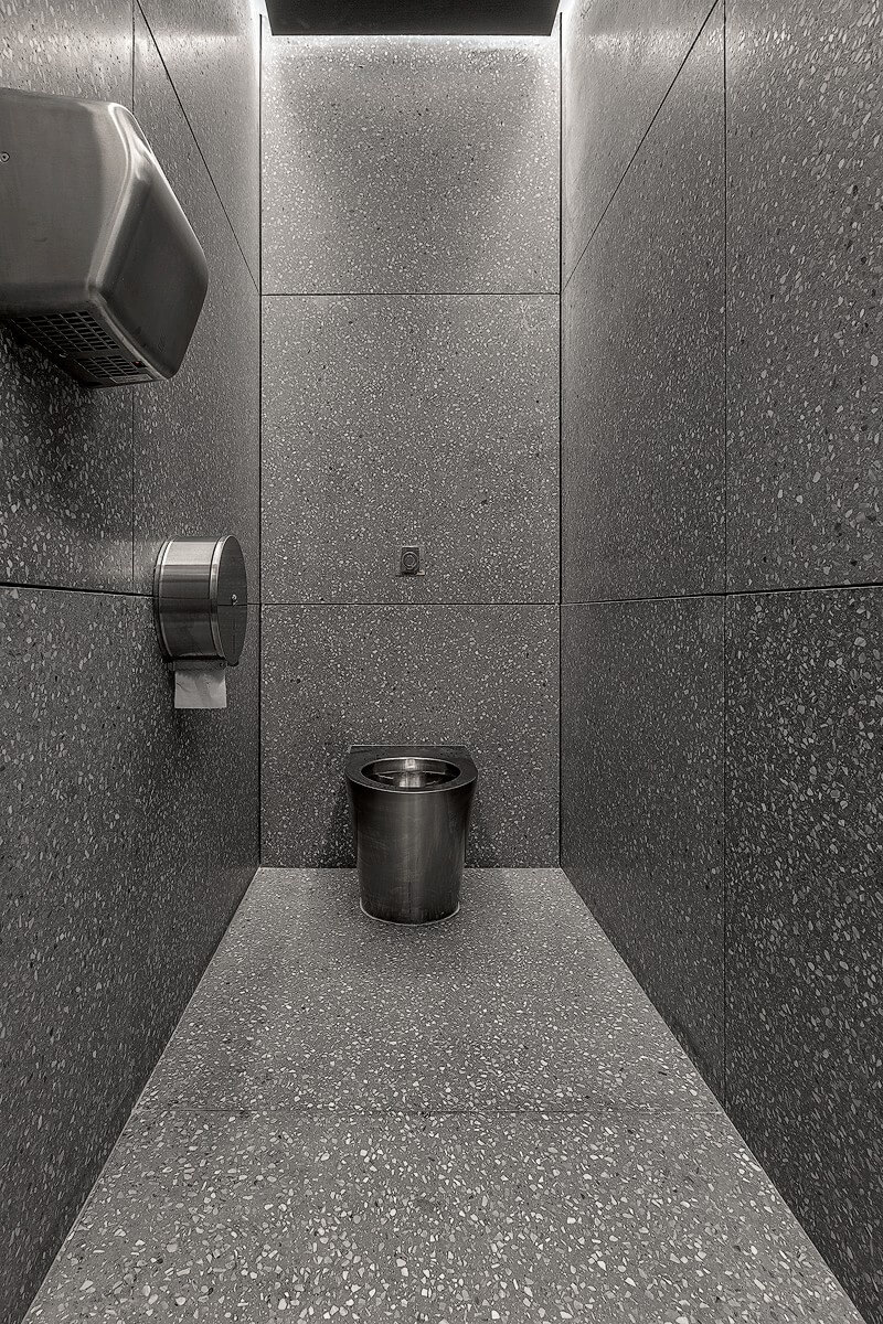 Compact restroom at Ecabs with dark terrazzo walls and flooring, stainless steel fixtures, and recessed ambient lighting.