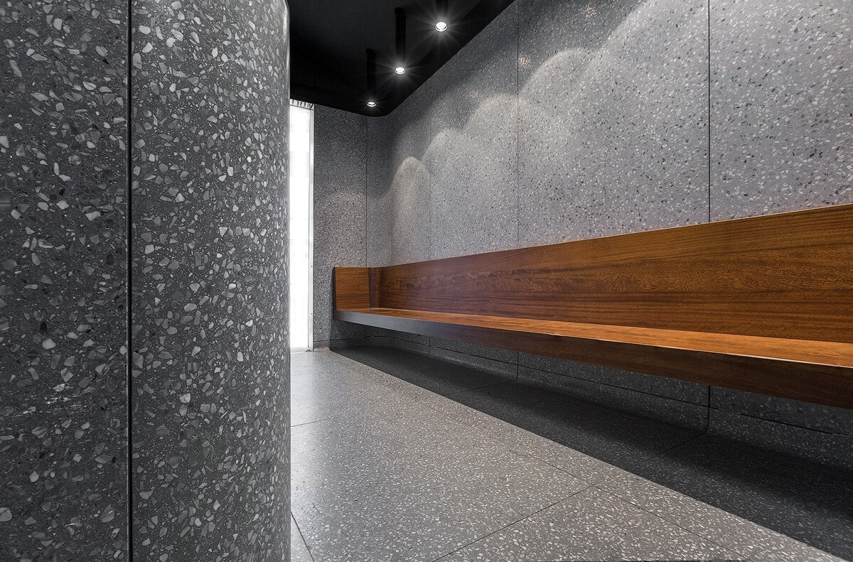 Close-up of the Ecabs waiting area featuring a floating walnut bench mounted against terrazzo-clad walls, with curved column detailing and recessed spotlighting above.