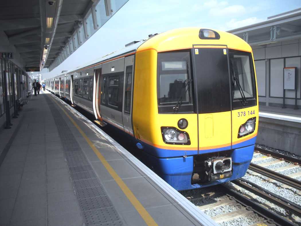 View of Hoxton station platform from across the tracks, showing London Overground roundels, signage, and minimalistic platform design with clean white and grey tones.