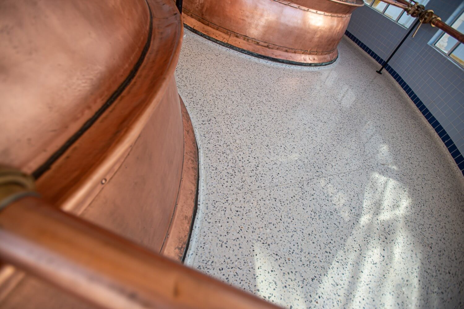 Detail view of the curved copper base of a brewing vat highlighting the seamless integration of the terrazzo flooring around it.