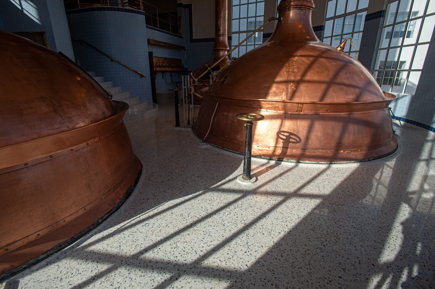 Sunlight casting shadows on the terrazzo floor beside restored copper kettles, showcasing the shine and texture of the surface.