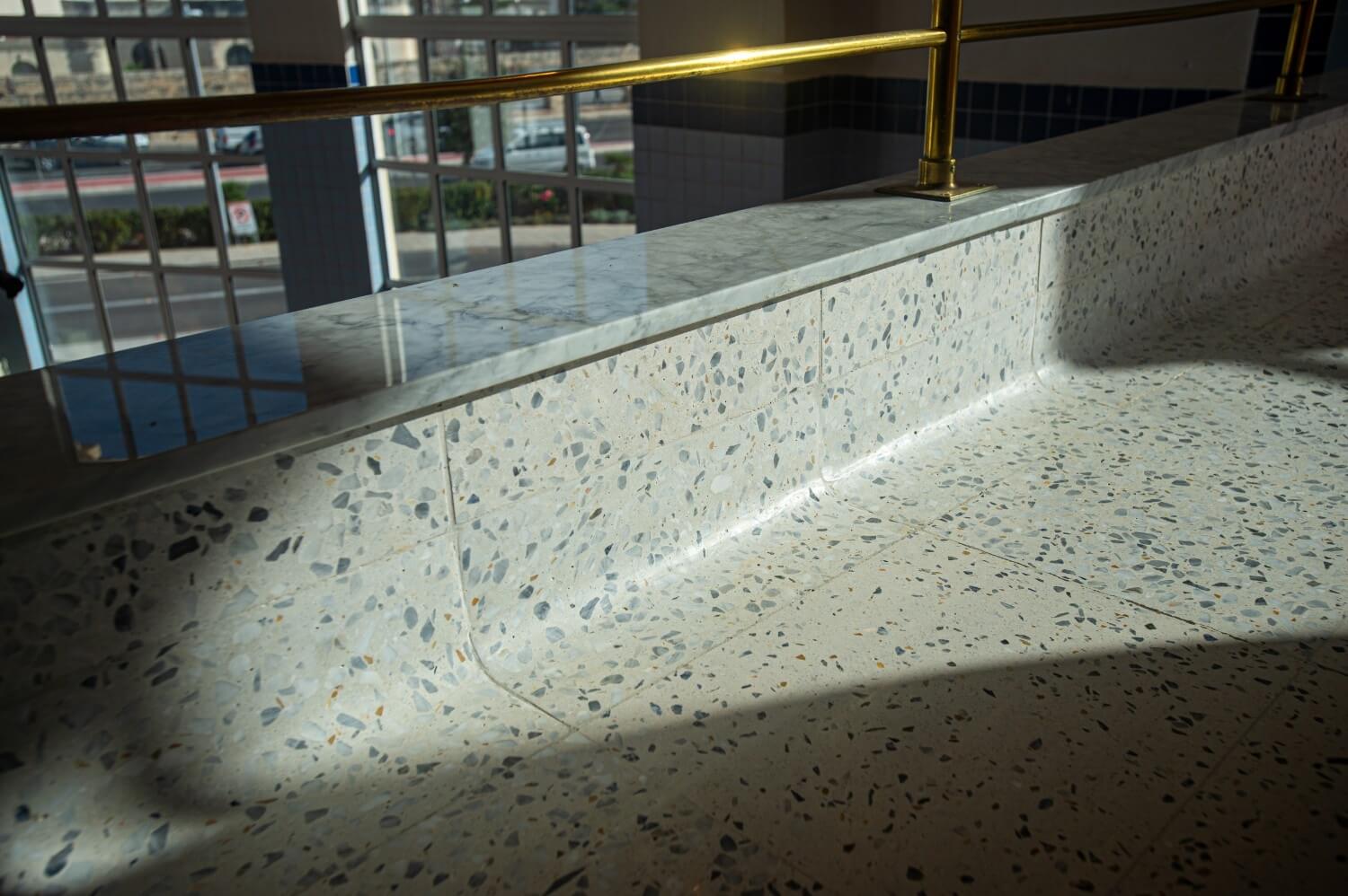 Close-up of a terrazzo-clad ledge with a marble top and brass railing, part of the brewery’s upper-level viewing area.