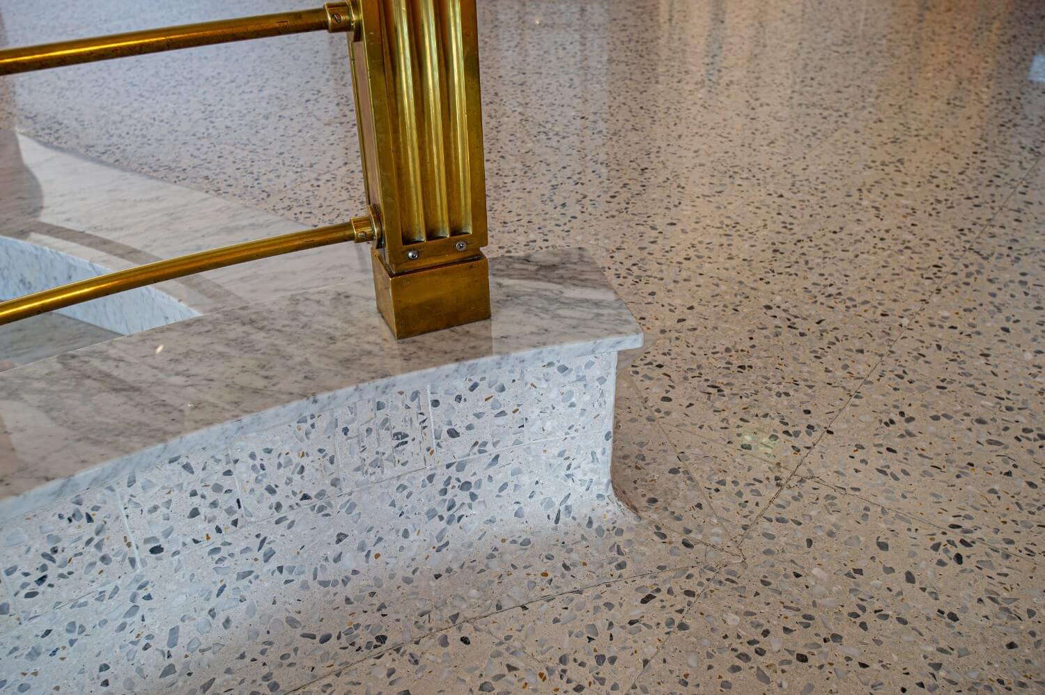 Close-up of terrazzo floor and base wall interface with marble railing post, showcasing the smooth curved detailing of the material.