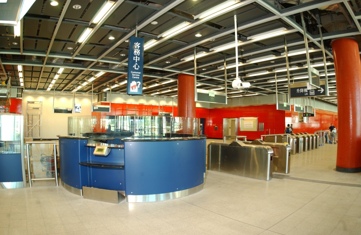 Customer service centre at Kowloon Station, showcasing a circular blue service desk, stainless steel ticket barriers, and overhead signage in both English and Chinese.